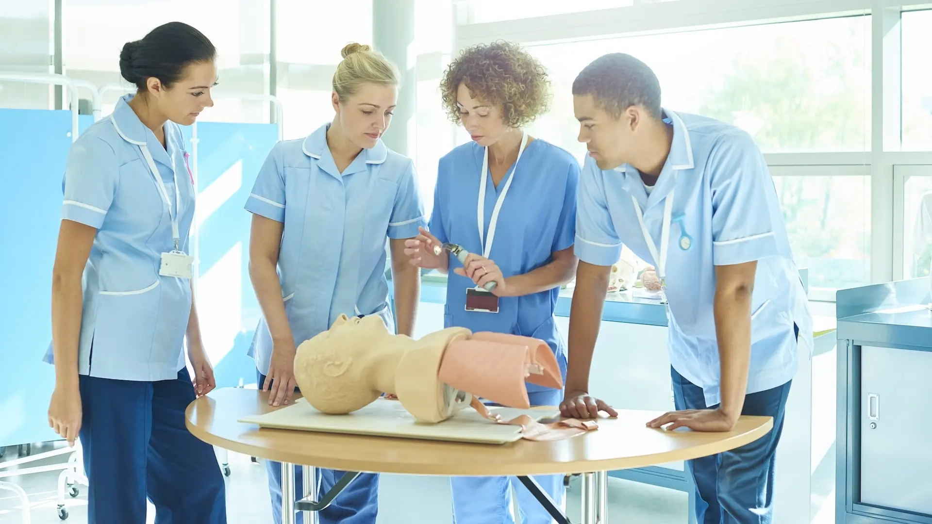 3 junior nurses being given a demonstration on a dummy by a senior nurse
