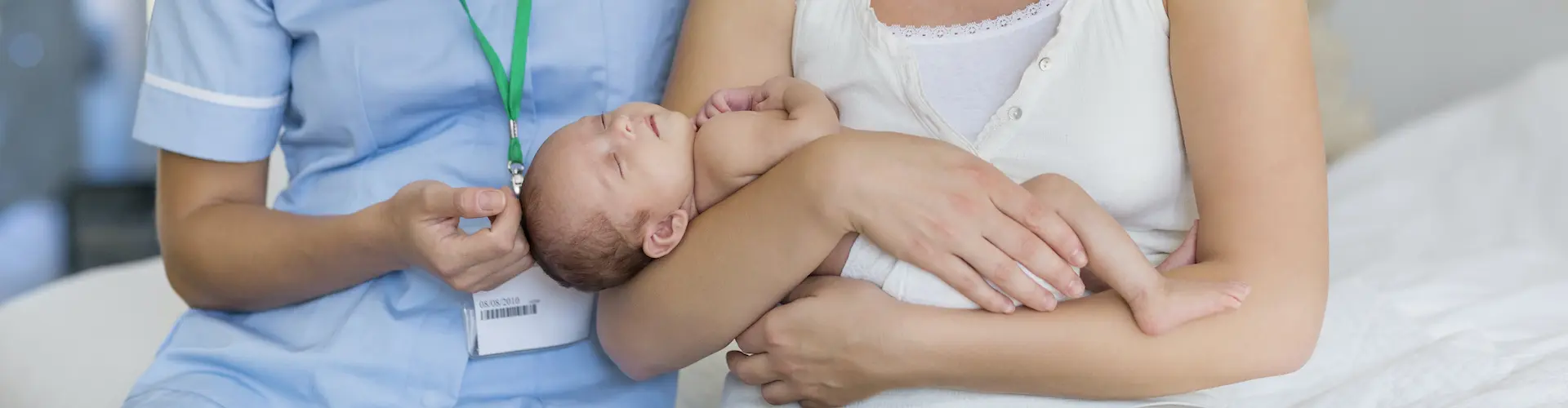 A mum holding her baby, beside a midwife