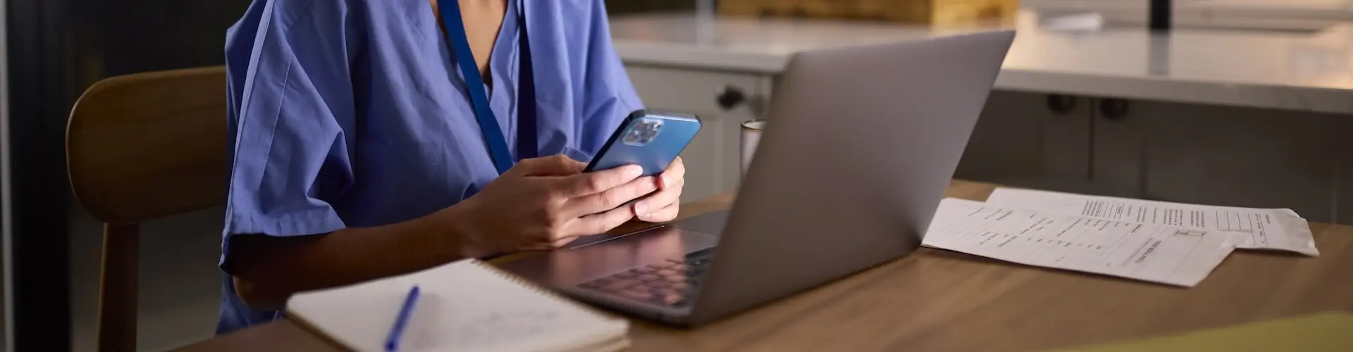 Nurse sitting at a desk looking at her laptop and phone