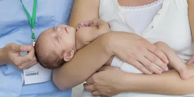 A mum holding her baby, beside a midwife