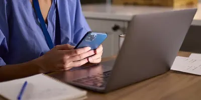 Nurse sitting at a desk looking at her laptop and phone